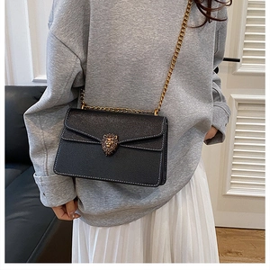 Detail of black pebbled leather crossbody bag with golden lion head buckle and white stitching