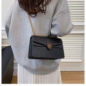 Detailed shot of black crossbody bag featuring a gold lion head buckle and chain strap
