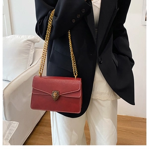 Close-up of red leather chain bag with golden lion head emblem on a fashion model
