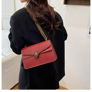 Detail of red pebbled leather crossbody bag with a vintage gold lion head emblem