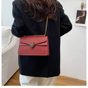 Detail of dark red lychee leather crossbody bag with golden lion head buckle on model