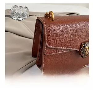 Detail of lion head hardware and white contrast stitching on brown pebbled leather bag