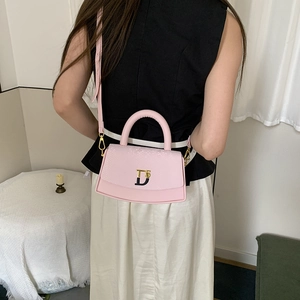 Crossbody view of light pink leather bag with snake-skin texture and gold logo