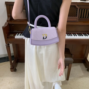 Lavender box bag with faux snakeskin texture and metallic clasp on a dark piano