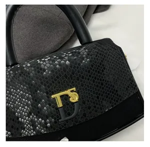 Close-up of snake skin texture and gold metal T5 logo on luxury black leather handbag