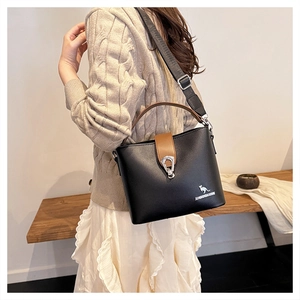 Detail of black pebbled leather bucket bag with brown handles and adjustable strap