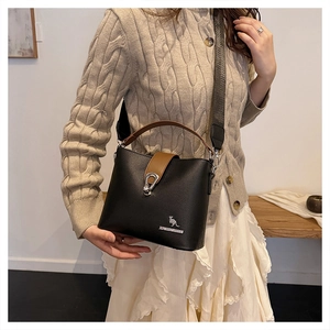Detail of black leather bucket bag with silver kangaroo logo and wide fabric strap