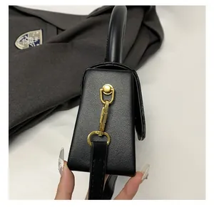Detail of gold-tone hardware and D-ring on black textured leather box handbag