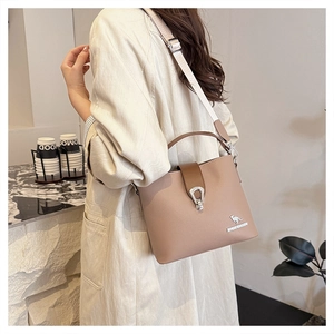 Close-up of light brown bucket bag with wide strap, silver kangaroo logo and buckle detail