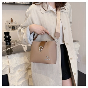 Detail of the light brown leather bucket bag with silver clasp and wide fabric strap
