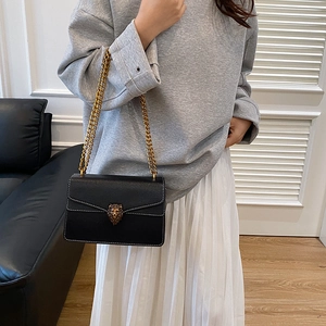 Black leather crossbody bag with lion head clasp and gold chain strap on female model