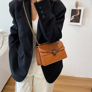 Brown leather crossbody bag with gold lion head buckle and chain strap shown on model