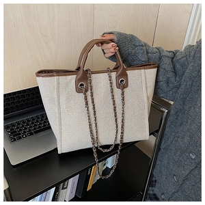 Close-up of white canvas tote bag with brown leather handles and decorative metal chain