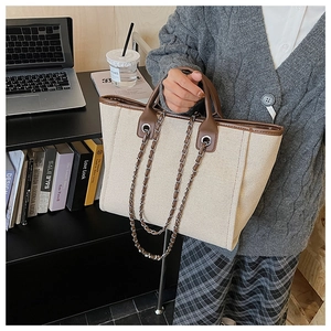 Detail of canvas tote bag with brown leather trim and metal chain strap in office setting