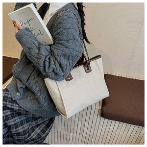 Detail of a large beige canvas tote bag with brown leather trim and chain shoulder strap