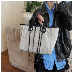 Detail view of canvas tote bag with leather trim and stylish metal chain strap