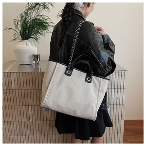 Detail of canvas tote bag with black leather trim and silver chain strap on model