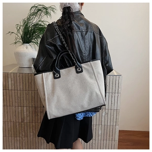 Detail of a large canvas tote bag with leather trim worn by a model in a leather jacket