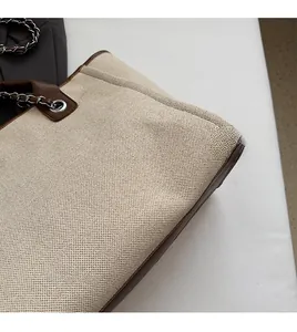 Detail of beige canvas tote with brown leather trim and silver metal chain strap