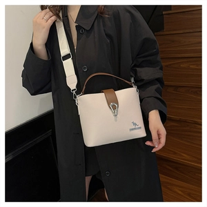 Detail of cream bucket bag showing brown leather handle, wide strap and silver twist lock