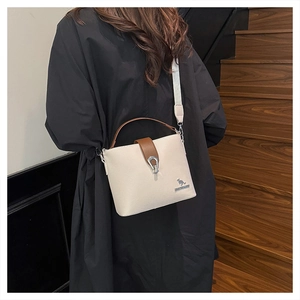 Detail view of cream bucket bag with brown leather accents and a wide woven strap