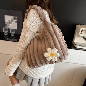 Brown fuzzy tote bag with a white flower charm worn by a model in a cozy room