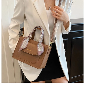 Detailed view of brown lychee leather handbag with decorative silk scarf and gold logo