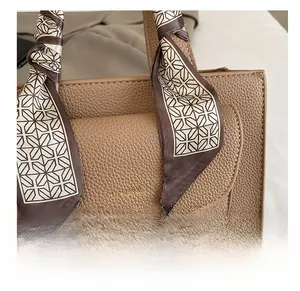 Close-up of brown pebbled leather handbag with logo and silk scarf wrapped handle