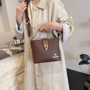 Brown leather bucket bag with kangaroo logo shown by model in beige trench coat