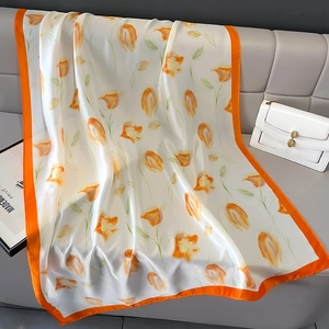 Elegant white silk scarf with orange tulip patterns draped over a grey leather sofa