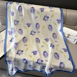 Detail of silk-like scarf with blue lily of the valley floral patterns on a leather sofa