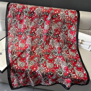 Detail of red paisley silk scarf draped on a sofa with smooth satin texture and black borders