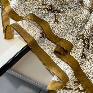 Dettaglio di sciarpa in seta con stampa paisley, finitura satinata bronzo e bordi larghi