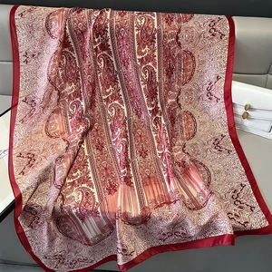 Dettaglio di sciarpa di seta rossa paisley su divano in pelle con borsa di lusso bianca