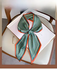 Détail d'un foulard en soie à fleurs orange avec broche perle sur un livre blanc