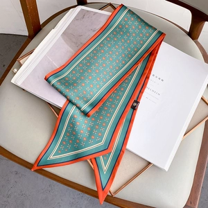 Foulard twilly en soie turquoise à motif floral avec bordure orange sur un fauteuil gris