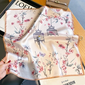 Elegant silk scarf with floral and bird prints displayed on a wooden surface