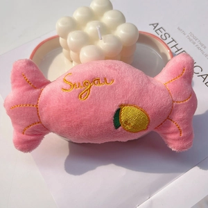 Pink plush candy-shaped dog toy with Sugar embroidery and lemon pattern on white desk