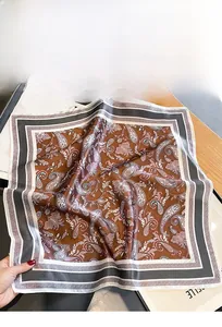 Detail of silk square scarf featuring dark brown paisley print and smooth satin texture