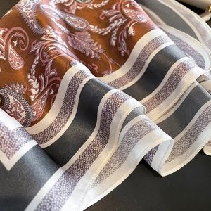 Detail shot of silk scarf showing glossy paisley patterns and premium satin texture