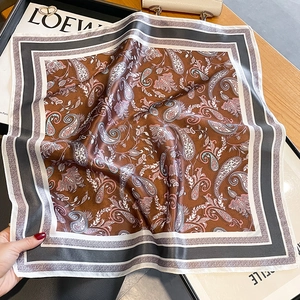 Caramel silk paisley square scarf with decorative borders draped on a warm wooden table