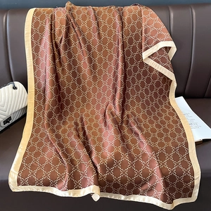 Elegant dark brown silk scarf with gold patterns draped on a leather sofa with accessories