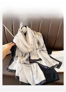 Close-up of elegant ivory silk scarf with lotus print and black borders on a dark surface