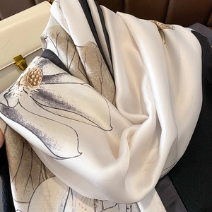 Elegant white silk scarf with lotus print draped over a stylish leather bag