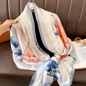 Floral print silk shawl with pink flowers and a white camellia brooch on a leather surface