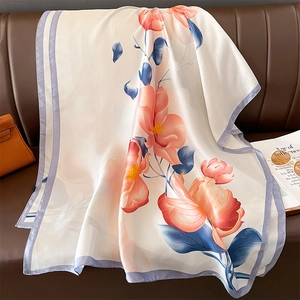 Elegant floral silk scarf with orange blossoms draped on a sofa for beach or sun protection
