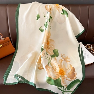 Detail of elegant silk scarf with yellow floral prints draped on a leather sofa