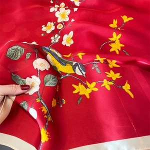 Macro detail of red silk scarf showing intricate floral and bird patterns in soft sheen