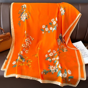 Macro detail of the smooth orange silk scarf featuring elegant bird and floral patterns