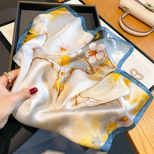 Elegant silk scarf with floral prints and blue edges displayed in a stylish setting